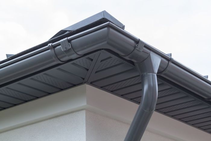 Close-up of gray gutters and downspout on a house roofline and soffit